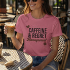 A woman wears a pink Caffeine & Regret Management t-shirt while holding an iced coffee.