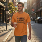 A man wears an orange Caffeine & Regret Management t-shirt while walking down a city street.