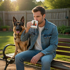 A man sits on a bench with a German Shepherd, drinking from a white ceramic Loyal Dog coffee mug.