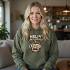 A woman wears an olive green hoodie featuring a cartoon coffee mug and Help! I Need Coffee!! text.
