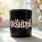 Black ceramic mug featuring the word GRANDMA in colorful Easter-themed letters with bunny ears.