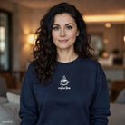 A woman wears a navy blue crewneck sweatshirt featuring a small white coffee cup graphic.