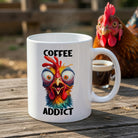 A white ceramic mug featuring a colorful, wide-eyed, frazzled chicken and the text Coffee Addict.