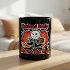A black ceramic mug featuring a stick figure illustration and the text Weekend Battle Me vs The Mug.