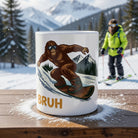 White ceramic mug featuring a snowboarding Sasquatch and the word BRUH in a snowy mountain setting.