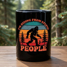 Black ceramic mug featuring a retro Bigfoot graphic and the text I'm Hiding From Stupid People.