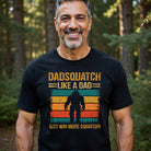 A man wears a black Dadsquatch t-shirt with a retro Bigfoot graphic and funny text.