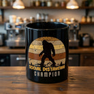 Black ceramic mug featuring a retro Bigfoot silhouette and Social Distancing Champion text.