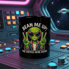 Black ceramic mug with a cartoon alien and the text Bean Me Up! The Coffee Here Sucks.