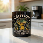 Black ceramic coffee mug featuring a cartoon frog and the text Caution Without Coffee I Have No Filter.