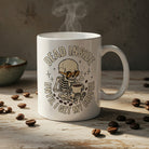 White ceramic mug featuring a skeleton drinking coffee with the text Dead Inside Until I Get My Coffee.