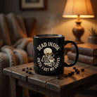 Black ceramic mug with a skeleton graphic and the text Dead Inside Until I Get My Coffee.