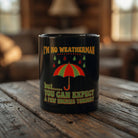 Black coffee mug with a colorful umbrella and a humorous weather-themed quote on a wooden table.
