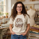 A woman wears an ivory t-shirt with a retro distressed coffee-themed graphic print.