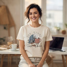 Woman wearing a cream-colored t-shirt with a graphic of a bird face-down in a coffee mug.