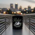 Black ceramic mug featuring a graphic of a frog relaxing on a lily pad with a coffee cup.