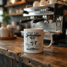 White coffee mug featuring a frog hanging from a branch above a crocodile with text.