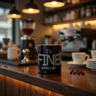Black ceramic coffee mug with 'I'm FINE' text design on a wooden cafe counter.