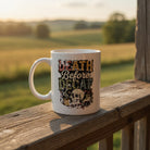 White ceramic mug featuring a skull graphic and the text Death Before Decaf on a wooden railing.