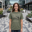 Woman wearing an olive green graphic tee with a coffee bean reclining on a vintage sofa.