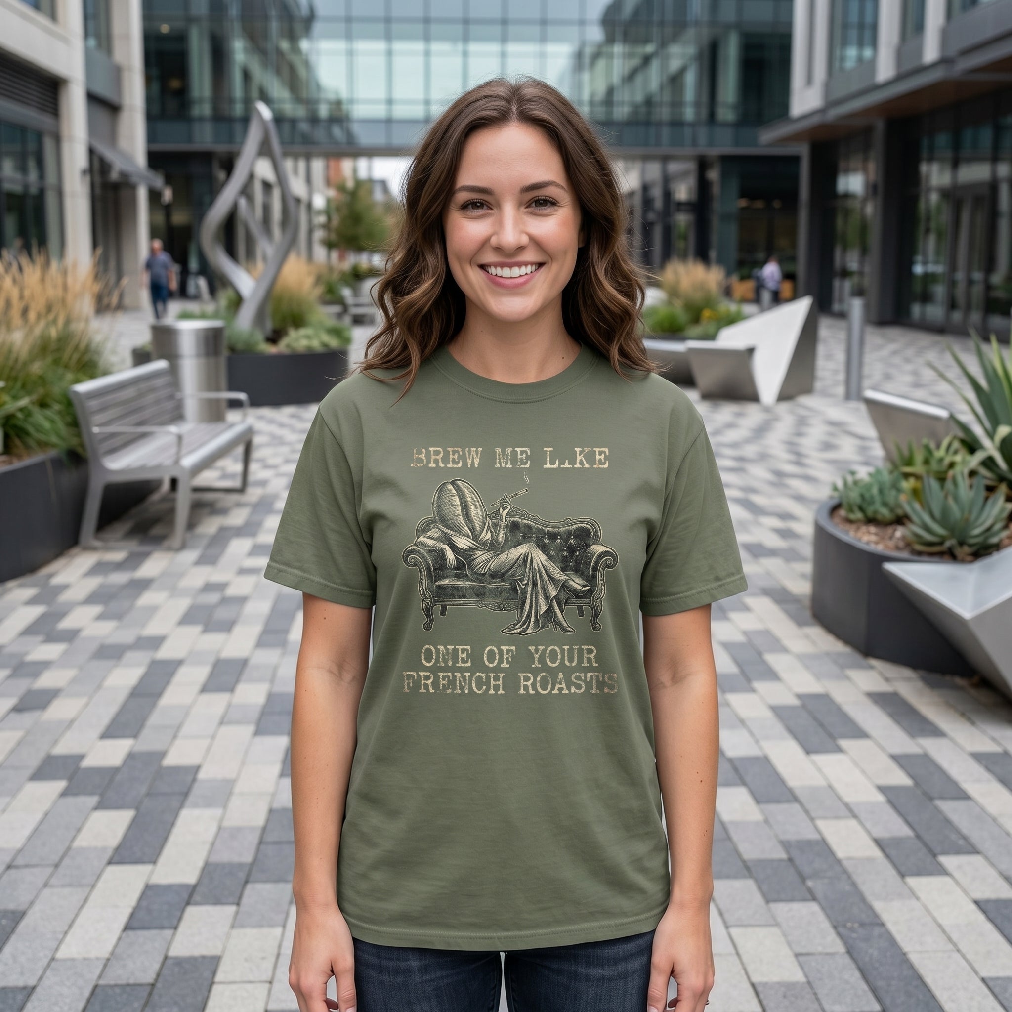 Woman wearing an olive green graphic tee with a coffee bean reclining on a vintage sofa.