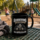 Black ceramic coffee mug with a skeleton graphic and text Surviving Fatherhood One Coffee At A Time.