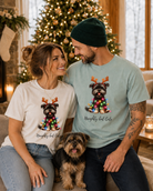 A man and woman wearing matching Yorkie Christmas graphic t-shirts with a Yorkie dog sitting nearby.