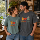A man and woman wearing Peace Love Coffee graphic tees in a cozy coffee shop setting.