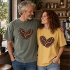 Man and woman wearing oversized coffee bean heart graphic tees in olive green and mustard yellow.