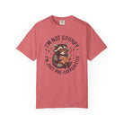 Coral-colored unisex t-shirt featuring a graphic of a raccoon reading a book with coffee.