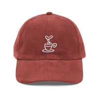 A rust-colored corduroy dad hat featuring a white embroidered coffee cup design on the front.