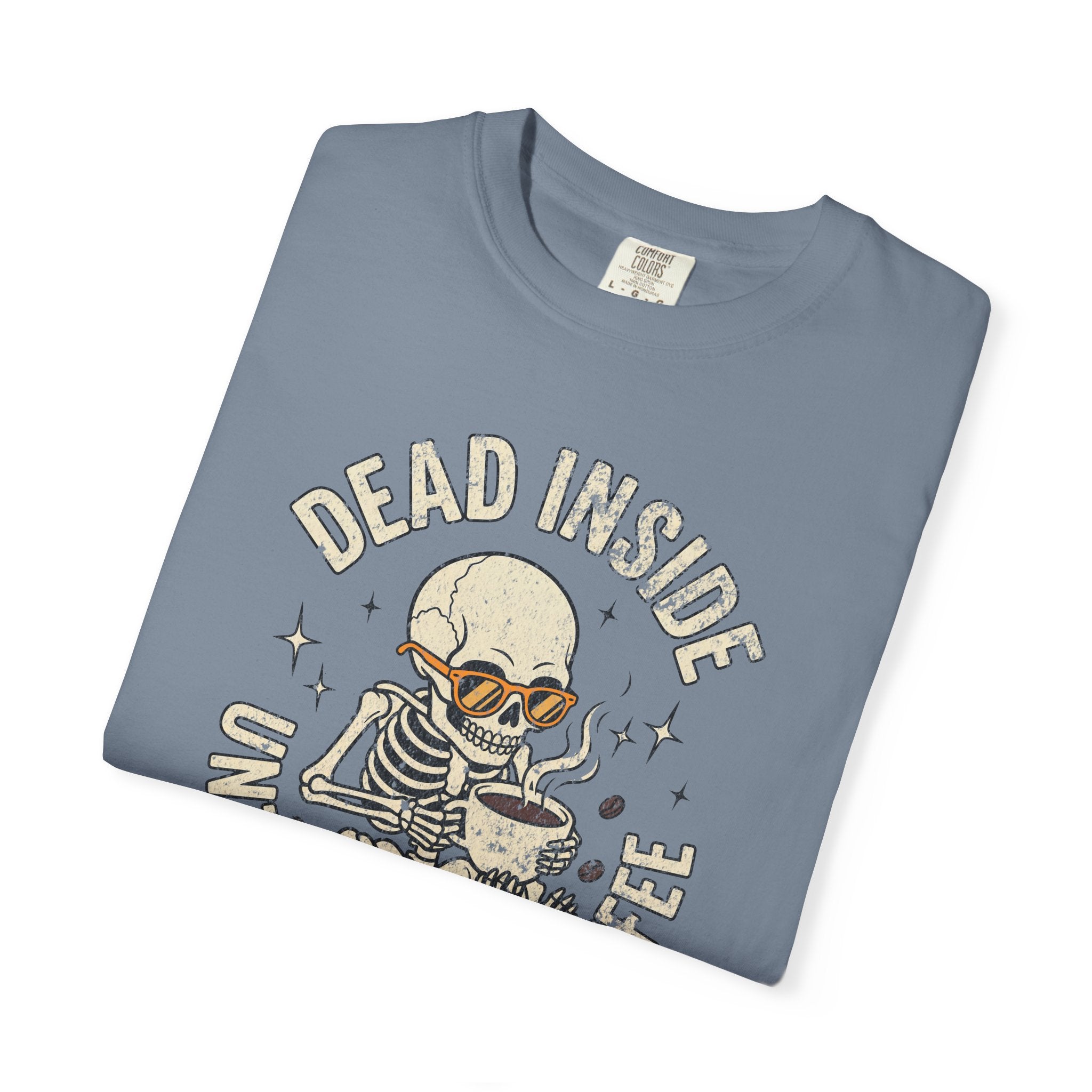 A folded blue t-shirt featuring a graphic of a skeleton wearing sunglasses and drinking coffee.