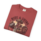 A folded red t-shirt featuring a graphic of a cowboy rooster pouring coffee into a mug.