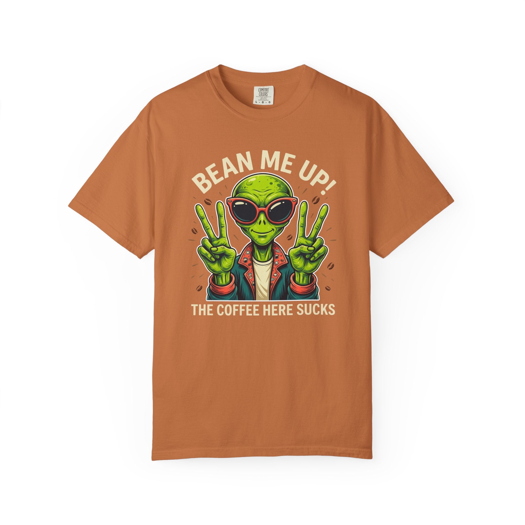 A rust-colored t-shirt featuring a green alien wearing sunglasses and making peace signs.
