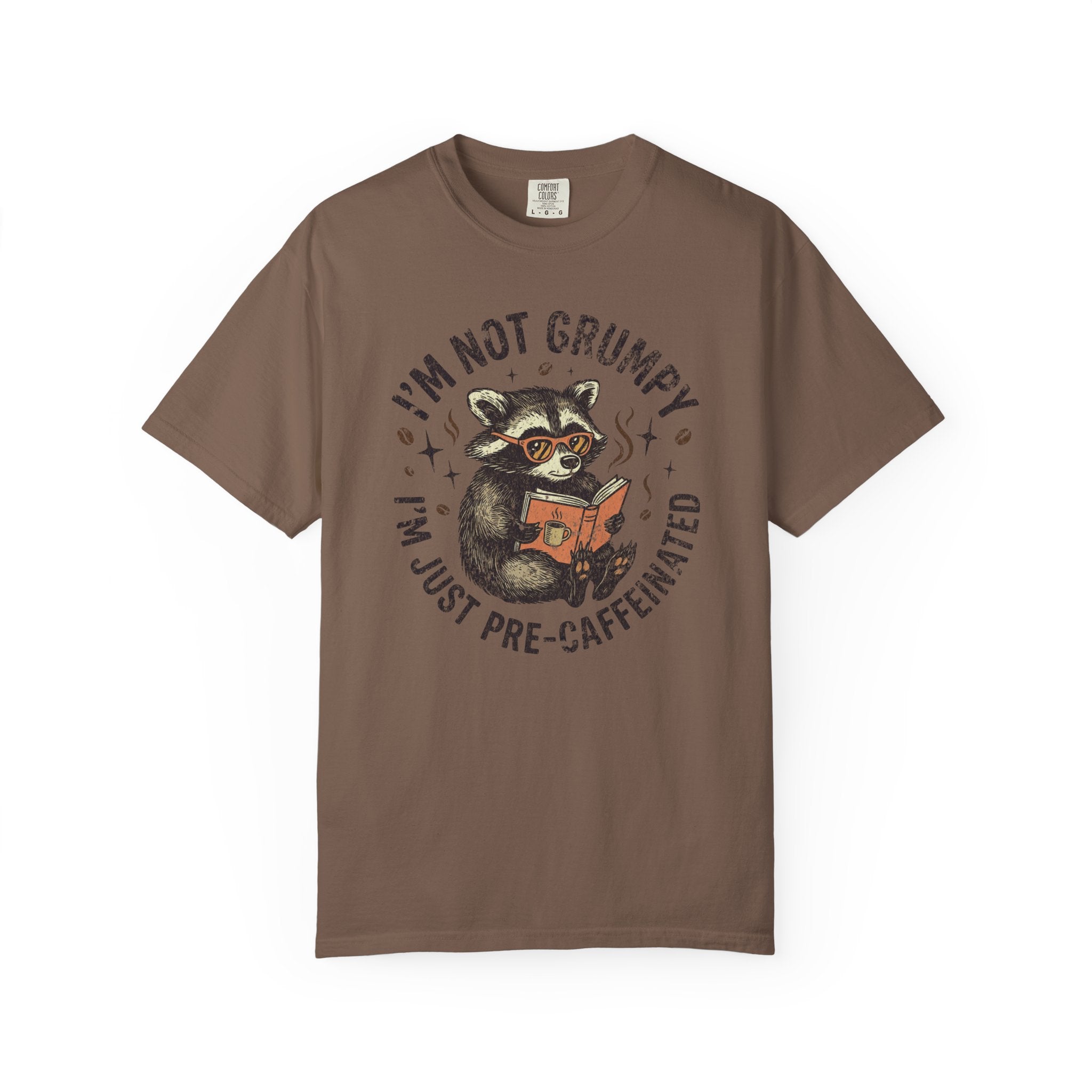 Brown unisex t-shirt featuring a raccoon wearing sunglasses and reading a book with coffee.