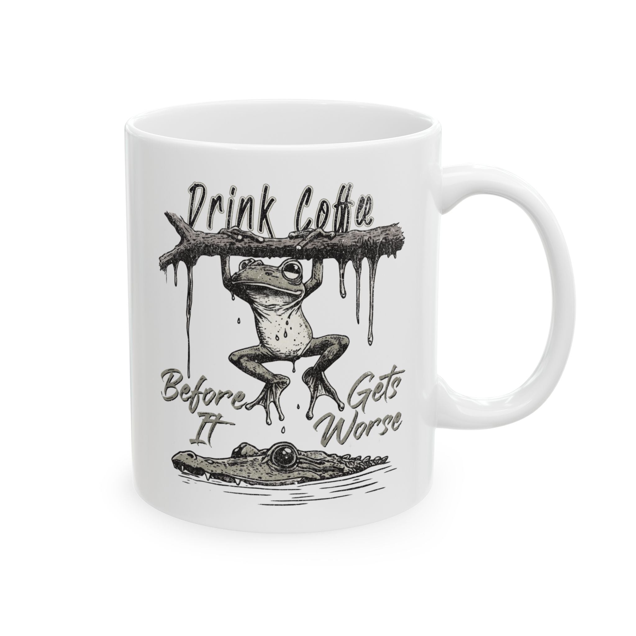 White ceramic coffee mug featuring a frog hanging from a branch above an alligator.