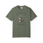 Olive green unisex cotton t-shirt featuring a raccoon holding a coffee cup with a skull design.