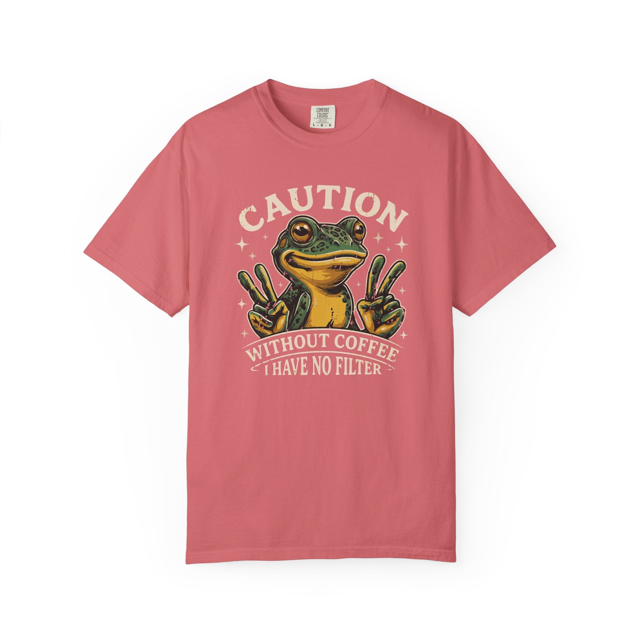 A coral-colored t-shirt featuring a graphic of a frog making peace signs with the text Caution.