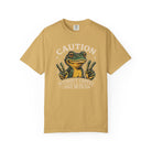 Mustard yellow t-shirt featuring a graphic of a frog making peace signs with the text Caution.