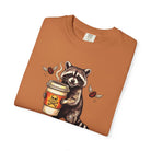 Orange Comfort Colors unisex t-shirt featuring a graphic of a raccoon holding a coffee cup.