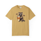 Mustard yellow Comfort Colors unisex t-shirt featuring a raccoon holding a coffee cup with a skull.