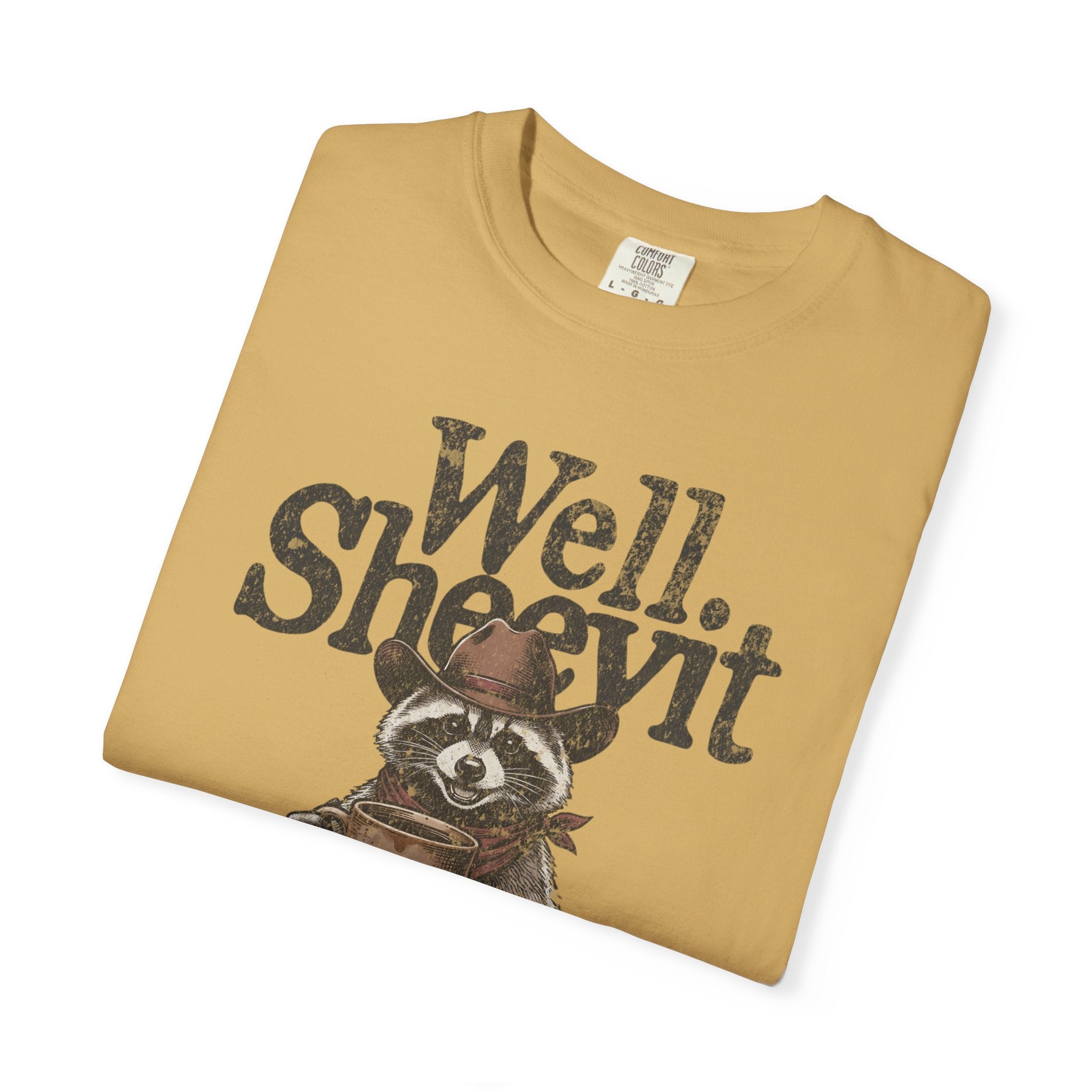 A tan t-shirt featuring a distressed graphic of a raccoon wearing a cowboy hat and holding coffee.