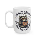 White ceramic coffee mug featuring a raccoon wearing glasses and reading a book.