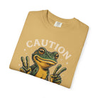 Folded mustard yellow t-shirt featuring a graphic of a frog making peace signs with the word CAUTION