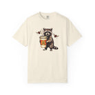 Cream-colored Comfort Colors unisex t-shirt featuring a graphic of a raccoon holding a coffee cup.
