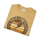 A folded tan t-shirt featuring a vintage-style graphic of a coffee bean and the text This Is A Very