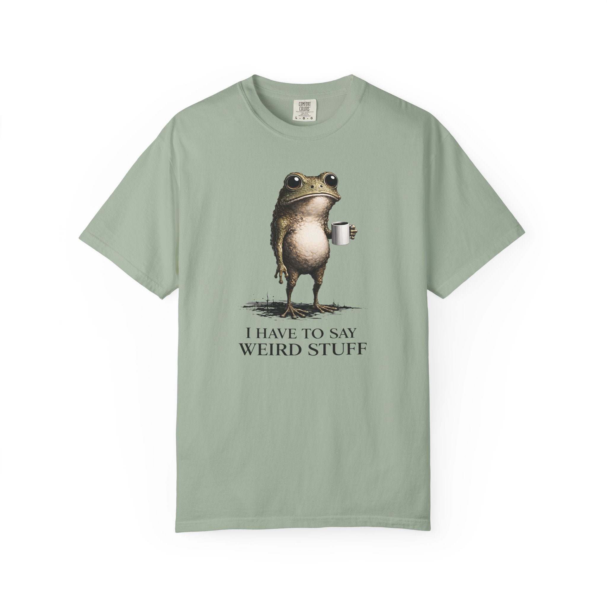 A sage green cotton t-shirt featuring a graphic of a frog holding a coffee mug with text below.