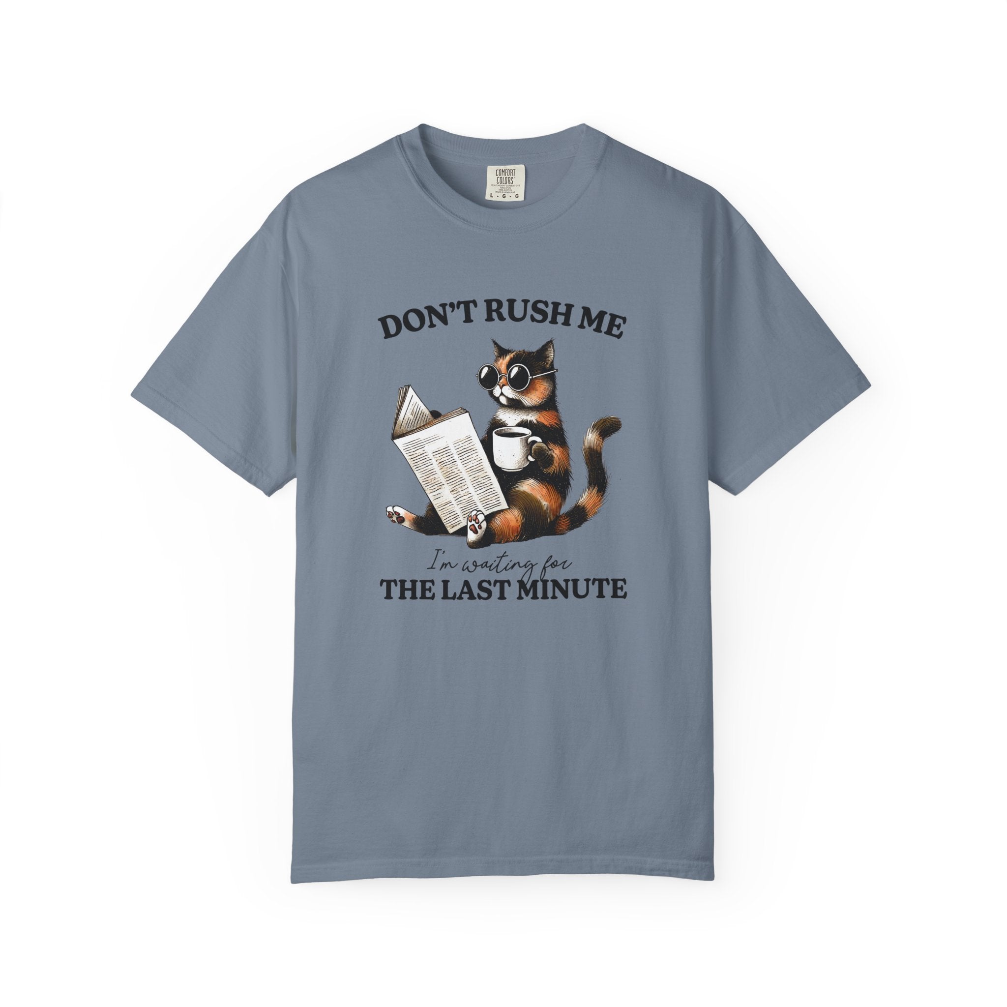 A blue garment-dyed t-shirt featuring a graphic of a cat wearing sunglasses, reading, and drinking.