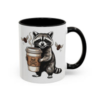 White ceramic mug with a black handle and interior, featuring a raccoon holding a coffee cup.