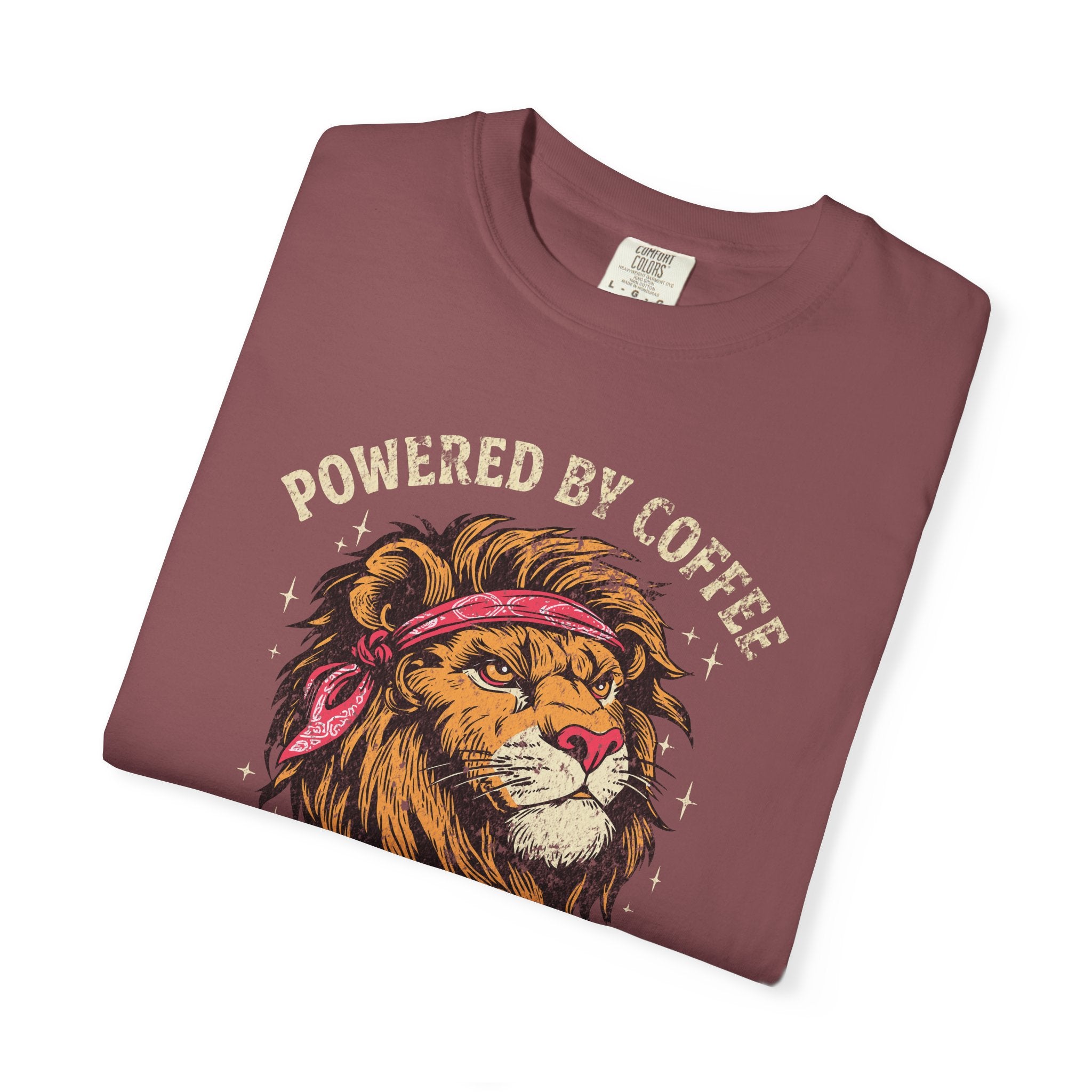 Folded maroon t-shirt featuring a graphic of a lion wearing a bandana with Powered by Coffee text.